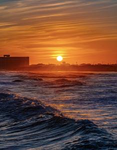 a sunset over the ocean with the sun setting at Salty Waves | Beach Cottage, Walk to Beach, Pool, Fenced Yard & Grill in Port Aransas