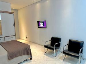 a room with two chairs and a bed and a tv at Garagem, Pátio Privativo - Apartamento Completo Moderno in Campo Novo do Parecis