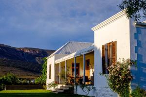 uma casa branca com montanhas ao fundo em Vrisch Gewagt Boutique Self-Catering Olive Farm em Prince Albert