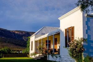 a white house with mountains in the background at Vrisch Gewagt Boutique Self-Catering Olive Farm in Prince Albert