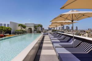 a pool with lounge chairs and umbrellas on a building at Dizengoff 99 by Isrotel Design in Tel Aviv