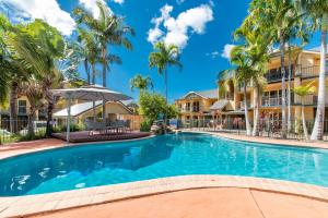 a swimming pool in front of a building with palm trees at Beach Court - Airlie Beach in Airlie Beach