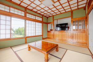 a room with a table and a tv and windows at ジャポニークハウス in Sanmu