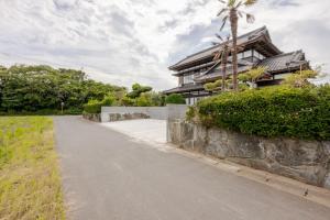 a house with a stone wall next to a street at ジャポニークハウス in Sanmu