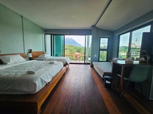 a bedroom with two beds and a desk and windows at Piney Stay ไพนี่สเตย์ เขาค้อ in Campson