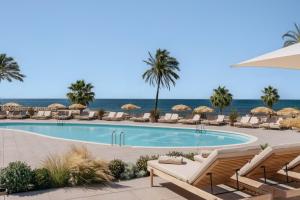a pool at the beach with chairs and umbrellas at ME by Meliá Sitges Terramar in Sitges
