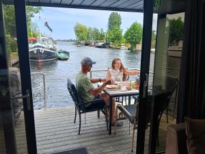 a man and a woman sitting at a table on a boat at Houseboat Enjoy with 200m Private Garden on the Lake in Vinkeveen