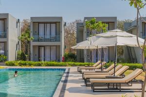 a pool with chaise lounge chairs and umbrellas at Vanam at Sasan in Sasan Gir