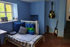 a blue room with a bed with pillows and a guitar at Tranquil Woodland Cottage by river Wye in Lydbrook