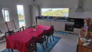 a dining room with a red table and a kitchen at Casas do Pargo- Casa A - Oak Tree House in Lombada Velha