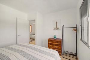 a white bedroom with a bed and a wooden dresser at A la Playa en San Agustín in Maspalomas