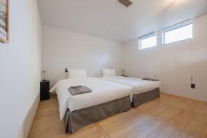 a white bedroom with two beds and a window at 椿森コムナStay in Chiba