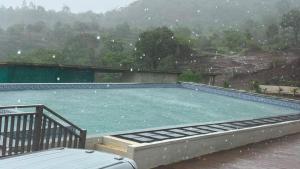 a large swimming pool in the rain with a view at Jashoda Dham Agro Tourism in Pune