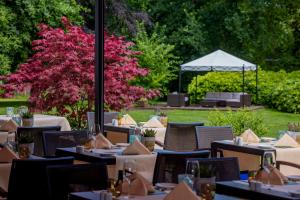 a restaurant with tables and chairs in a garden at Parkhotel Hohenfeld Münster in Münster