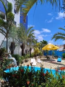 a pool with chairs and an umbrella and palm trees at Pousada Chácara Porto do Sol in Jacumã