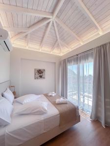a white bedroom with a bed and a large window at euphoria villas - Gaia & Aura in Agios Nikitas