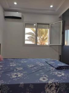 a bedroom with a bed with a blue blanket and two windows at Dar saber in Sfax