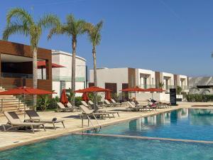 a swimming pool with chairs and umbrellas and palm trees at Grand Dominium in Agadir