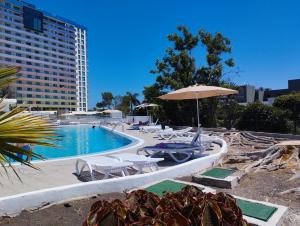 a swimming pool with an umbrella and chairs and a table at Ocean View Deluxe Studio with Sunset Balcony and Pool Playa Paraiso in Playa Paraiso