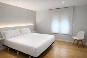 a bedroom with a white bed and a white chair at O Lar de LUCI in Nigrán