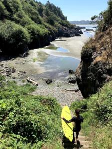 a person walking down a hill with a yellow surfboard at Rock Rose Cottage in Trinidad