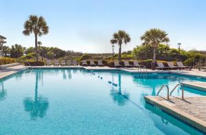 a large swimming pool with chairs and palm trees at Ocean Creek Resort in Myrtle Beach