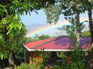 un arco iris sobre una casa con techo rojo en Cabañas La Pradera en Monteverde