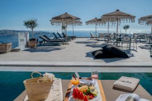 a table with a plate of food next to a pool at Apeiron Blue Santorini by Apeiron Hotels in Fira