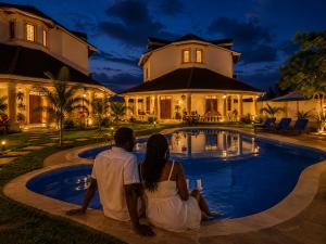 a couple sitting next to a swimming pool in front of a house at Greenfield Villa D- Diani in Diani Beach