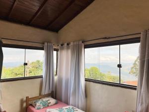 a bedroom with a bed and two large windows at Chalés do Chá in Lavras Novas