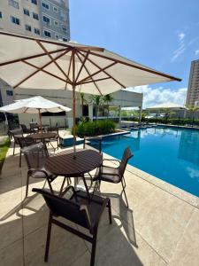 a table and chairs with an umbrella next to a pool at Auréa Residência - a 500 m da Praia in Cabedelo
