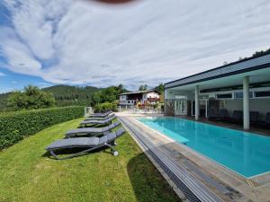 a pool with lounge chairs next to a house at Panorama Hof Sereinig in Sankt Oswald