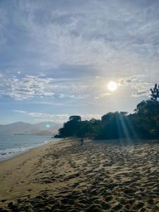 a sandy beach with the sun in the sky at Zion Cottage in Paraty