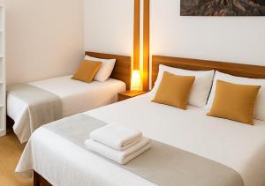 two beds in a hotel room with white and orange pillows at Kariokas Hospedagem in Águeda