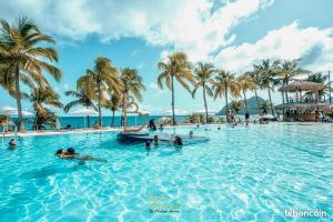 people in a swimming pool at a resort with palm trees at Appartement Rêve Clair in Le Diamant