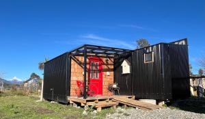 a black tiny house with a red door at Casita Loica in Chaitén