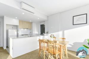 a white kitchen with a wooden table and chairs at Asquith 2BR Apt Secure Underground Parking in Asquith
