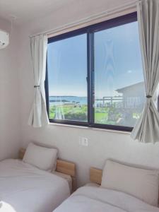 two beds in a room with a large window at guest house ALO in Miyako-jima