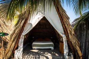 a bed in a straw tent under a palm tree at Tribu Hostal in El Paredón Buena Vista