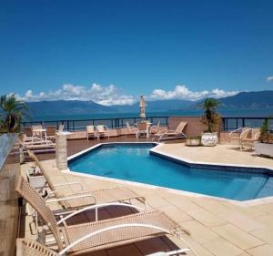 a swimming pool with chairs and a view of the water at Flat Beira Mar Caraguatatuba in Caraguatatuba