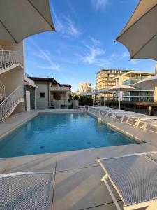 a large swimming pool with chairs and a building at Hotel Margherita in Lido di Jesolo