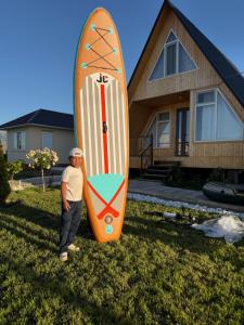 a man standing next to a surfboard in front of a house at Guest House Archa in Tong