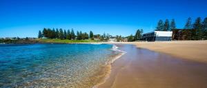a beach with the ocean and a building in the background at Ocean Tracks in Kiama +6 photos