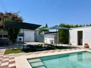 a pool with two umbrellas and a patio with chairs and a table at Villa El Carmen in Sanlúcar la Mayor