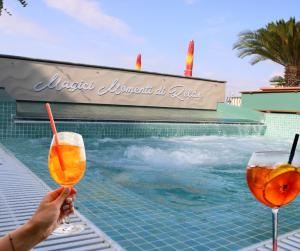 a person holding two drinks next to a swimming pool at HOTEL AURORA in Cattolica