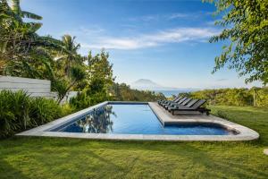 a swimming pool with two lounge chairs and the ocean at Villa Panorama in Nusa Penida