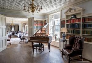 a living room with a piano and a table at Chilston Park Hotel in Maidstone