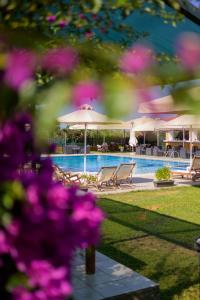 a swimming pool with chairs and umbrellas and purple flowers at Stomio Villague in Filiatra