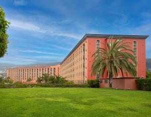 a large red building with a palm tree in front of a field at Hotel Las Águilas Tenerife, Affiliated by Meliá in Puerto de la Cruz