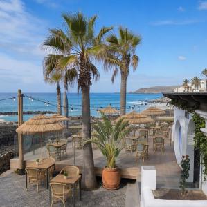 a patio with tables and palm trees and the ocean at Sands Beach Resort in Costa Teguise